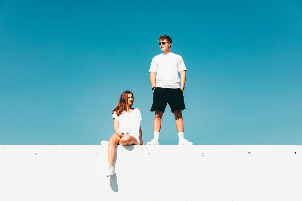 Eine Frau in weiß und ein Mann im weißen tshirt und schwarzen shorts stehen auf einer weißen Wand