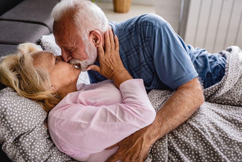 Ein älteres Paar liegt im Bett und küsst sich