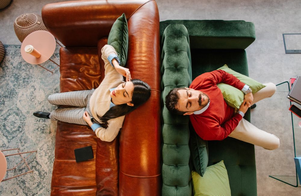 Zwei Sofas stehen mit der Rückenlehne aneinander. Auf dem linken Sofa sitzt eine Frau, auf dem rechten Sofa ein Mann.