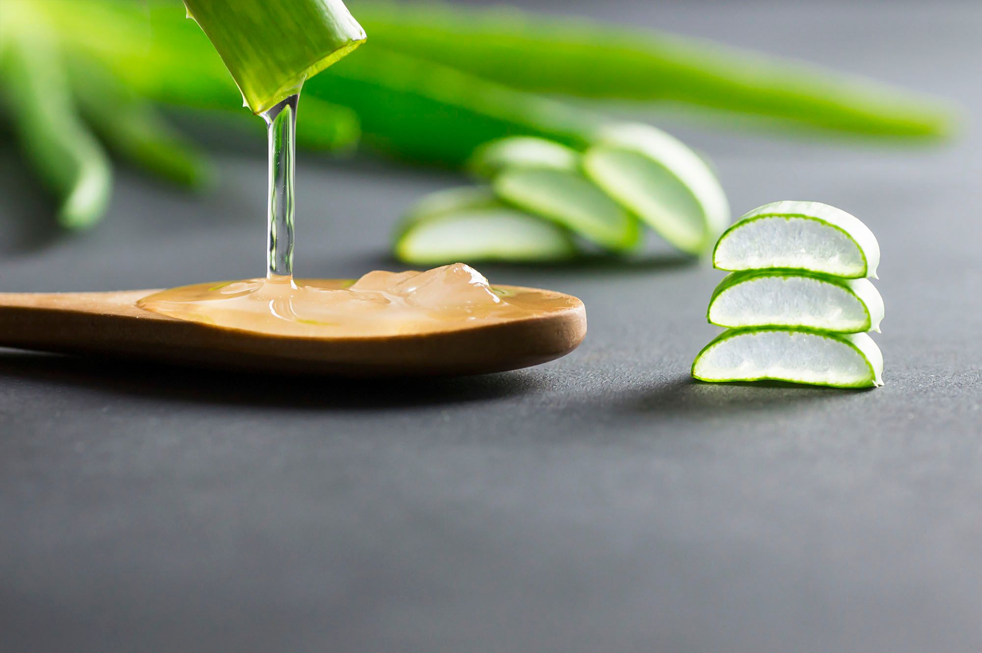 Gel einer Aloe Vera, das auf einen Holzkochlöffel fließt mit Aloe Vera im Hintergrund