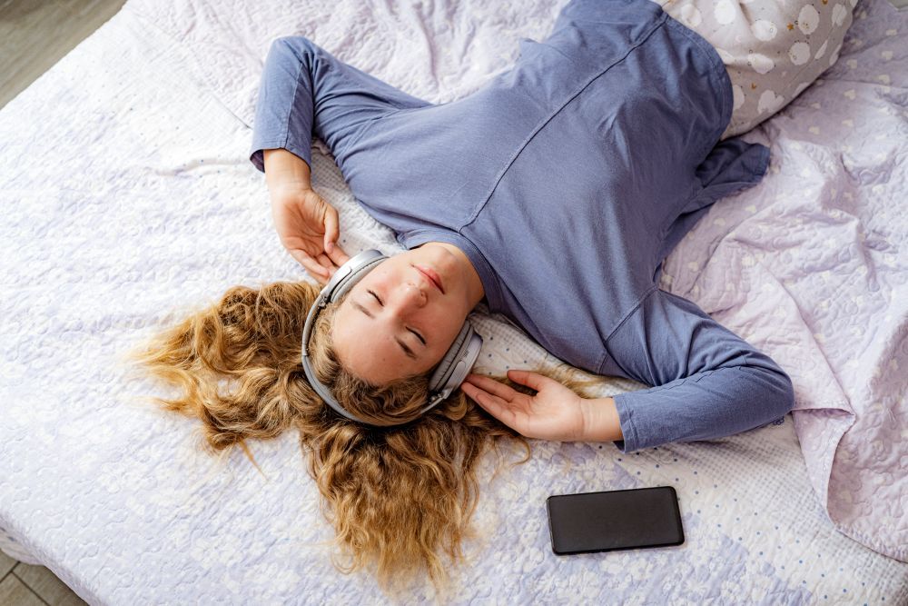 Ein Mädchen liegt im Pyjama im Bett und hört Musik auf ihren Kopfhörern. 