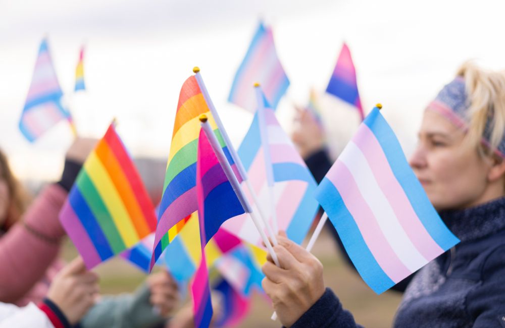 Eine Person hält viele Regenbogenflaggen und die trans* Flagge in der Hand