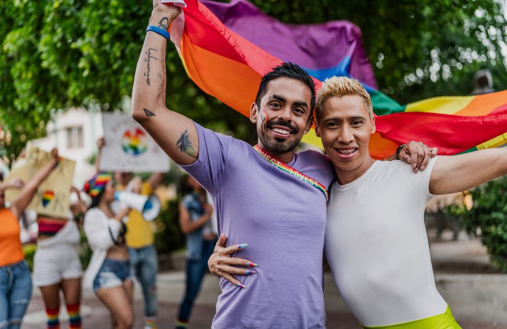 Zwei Männer stehen Arm in Arm und schwenken eine Regenbogenflagge.