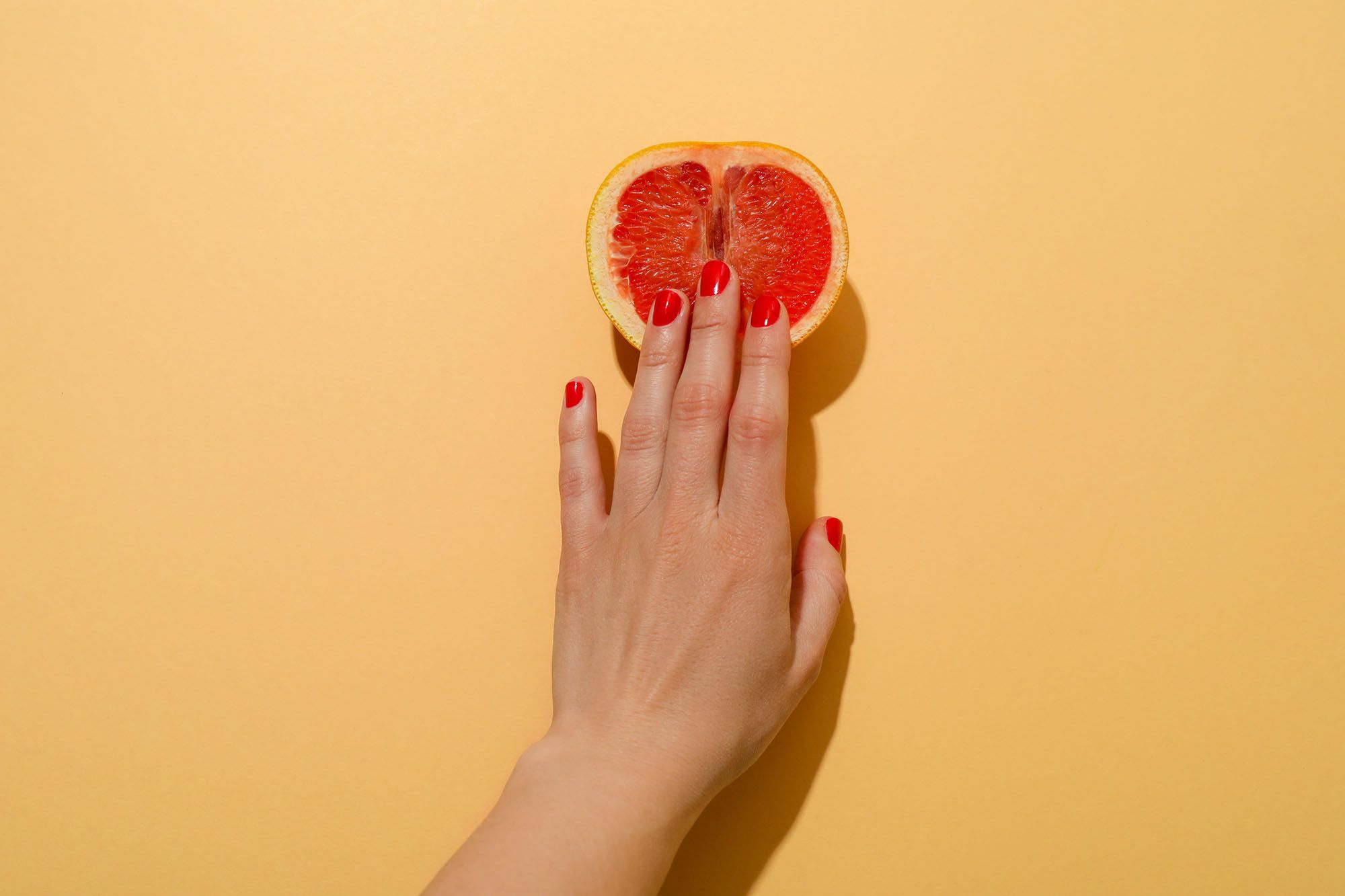 Halbe Grapefruit auf gelbem Hintergrund, die von einer Hand berührt wird