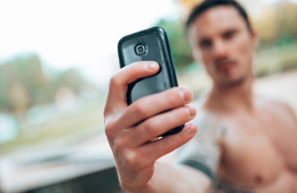 Ein Mann macht mit seinem Handy ein Selfie von seinem nackten Oberkörper