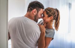 Frau in grauem Shirt und Mann in weißem Shirt, der die Frau im Arm hält und die sich anlachen