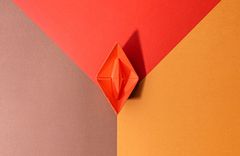 Origami-Figur in Rot, geometrisch platziert auf mehrfarbigem Hintergrund in Rot-, Braun- und Orangetönen