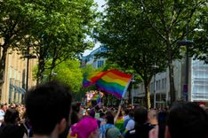 Viele Menschen sind während des Christopher Street Days auf der Straße, in der Mitte wird eine Regenbogenflagge geschwenkt.