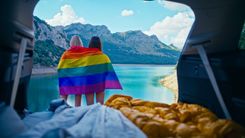 Zwei Frauen haben eine Regenbogenflagge um sich gelegt und stehen vor einem See.