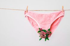 Eine rosa Unterhose hängt an einer Wäscheleine, in ihrem Schritt sind Blumen befestigt