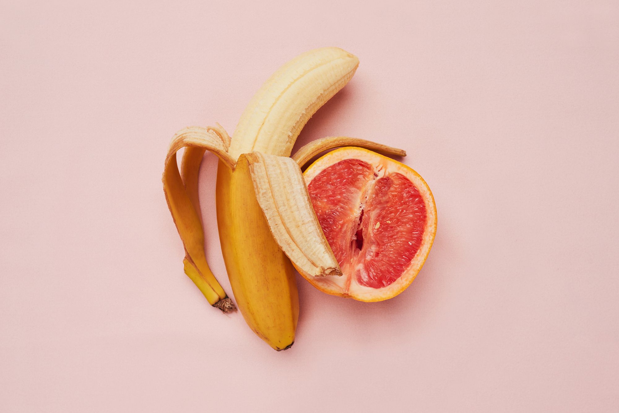 Halb-geschälte Banane und halbe Grapefruit auf einem rosa Hintergrund